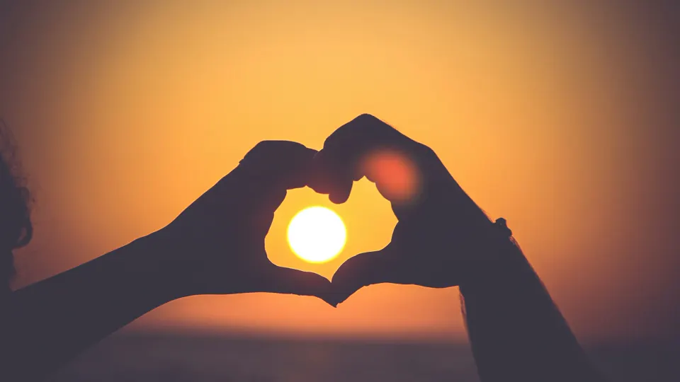 Two adults make a heart shape at sunset