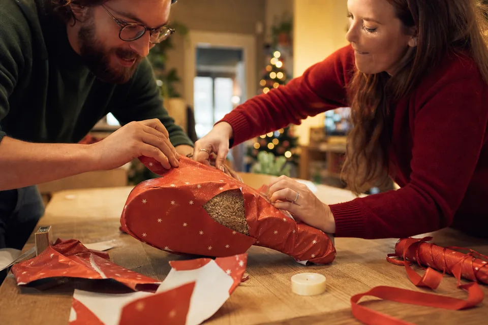 Two adults racing to wrap an awkwardly shaped Christmas gift